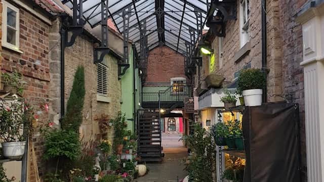 Free car park in Tickhill, Yorkshire, featuring a glass-roofed walkway and vibrant flower displays along the path.