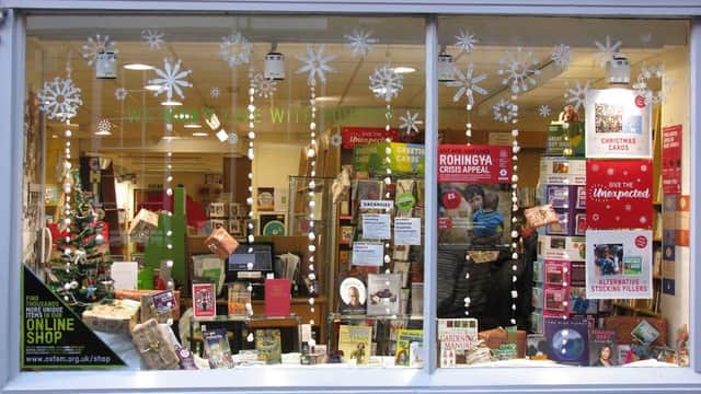 Oxfam Bookshop window display with books, decorations, and a Christmas tree, promoting various charity items.