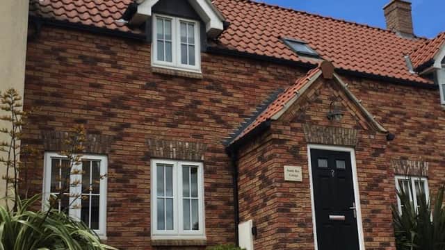 Charming brick cottage with a black door, white windows, and lush greenery under a blue sky in Sandy Bay, Filey.