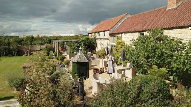 Charming lodge surrounded by greenery, outdoor seating, and a rustic stone building under a cloudy sky.