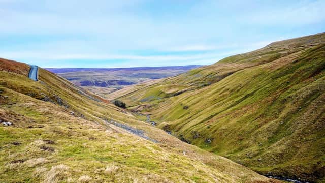 Rolling green hills and a winding road through the Yorkshire Dales, with a river flowing in the valley below.