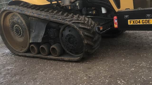 Yellow Challenger tractor with tracks parked on a gravel surface, showing muddy wheels and nearby machinery.