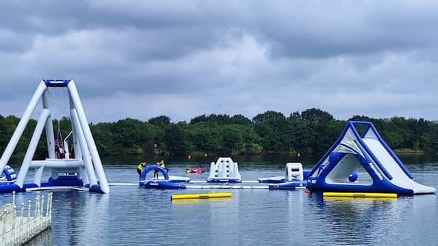 Inflatable water attractions on a lake with cloudy skies and trees in the background.