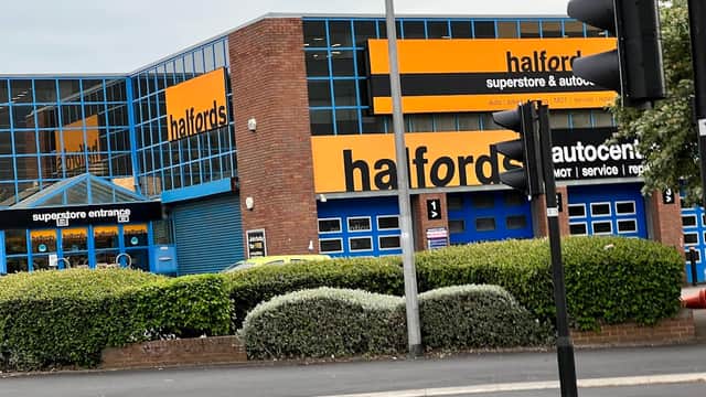 Halfords store with blue doors and windows, orange signage, and a green hedge in front, located on Meadow Lane, Leeds.