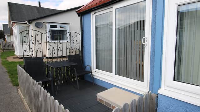 Blue holiday chalet with a patio, black chairs, and a small table, surrounded by a wooden fence in Wilsthorpe.