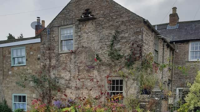 Stone cottage with colorful flower pots, ivy, and a house number 6, set against a cloudy sky.