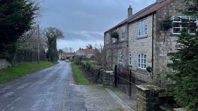 Stone cottage along a quiet road, surrounded by greenery and trees under a cloudy sky in Fadmoor, Yorkshire.