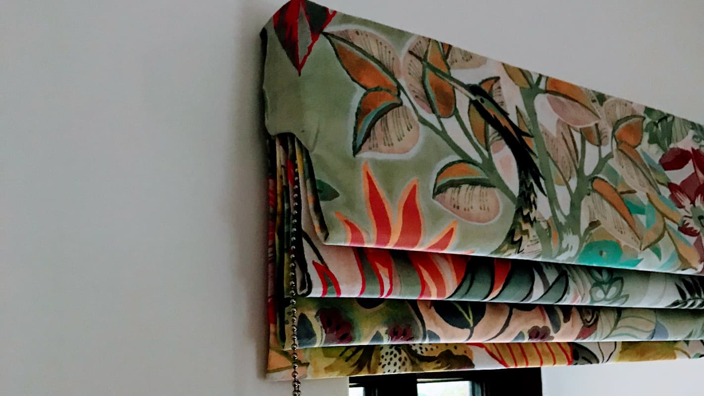 Colorful patterned Roman shades hanging above a window, showcasing floral and botanical designs.