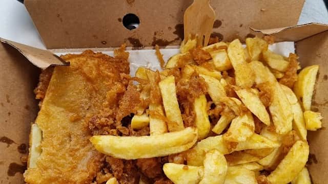 Golden-brown fish fillet with crispy batter alongside a generous serving of golden fries in a takeaway box.