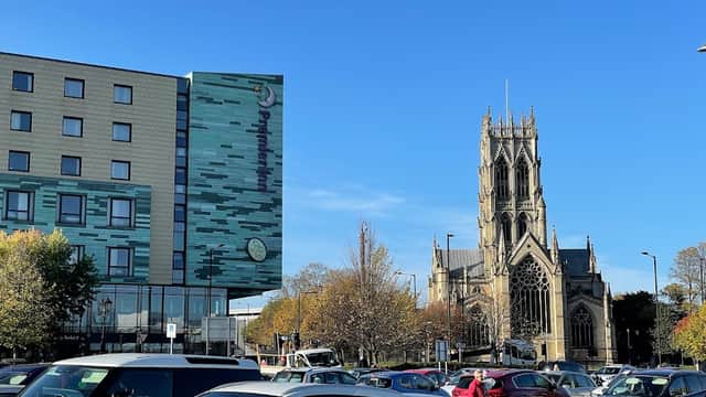 Pay & Display car park with cars, modern building, and a historic church under a clear blue sky in Doncaster.