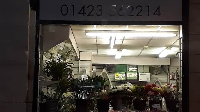 Storefront of Blamey's Florist, featuring a variety of flowers and plants displayed outside and a lit interior.