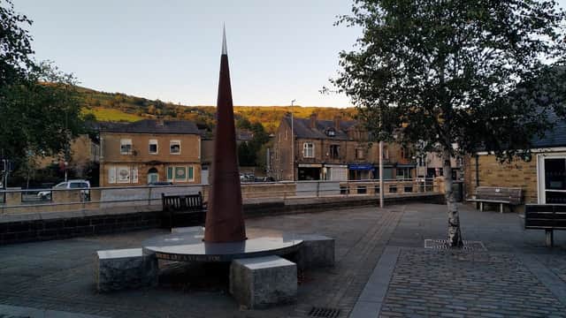 St. Michaels Square features a tall metal sculpture, stone benches, and buildings with a hillside backdrop in Chiserley, Yorkshire.