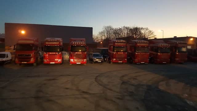 W Metcalfe & Sons Ltd trucks lined up in a yard at dusk, with a few parked vehicles and trees in the background.