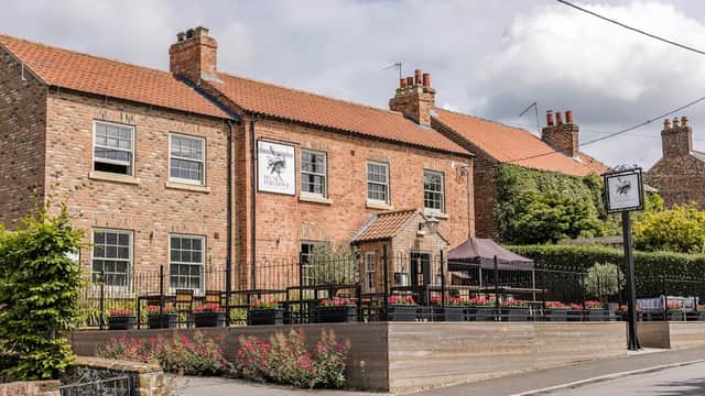 Brick building with a sign for "Plum & Partridge," outdoor seating, and flower beds in a quaint village setting.