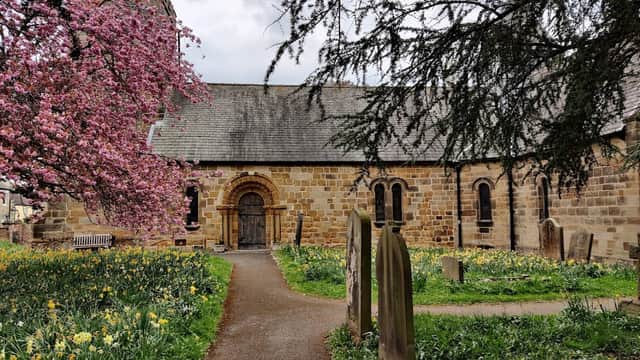 St Oswald's Church surrounded by blooming cherry trees and daffodils, with a stone path leading to the entrance.