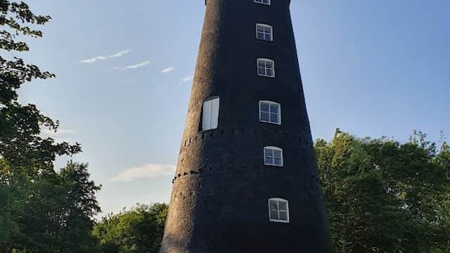 Black tower with windows, surrounded by green grass and trees under a clear blue sky.