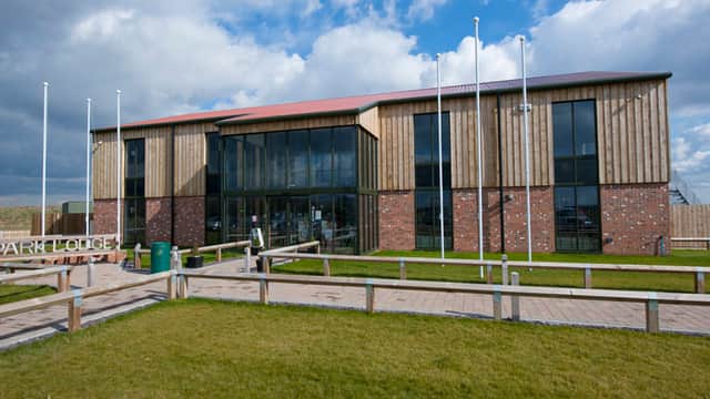 Modern building with wooden and brick facade, large glass windows, surrounded by green grass and flagpoles.