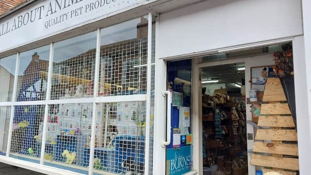 Pet shop exterior with a sign, display of pet products, and a wooden display stand outside the entrance.