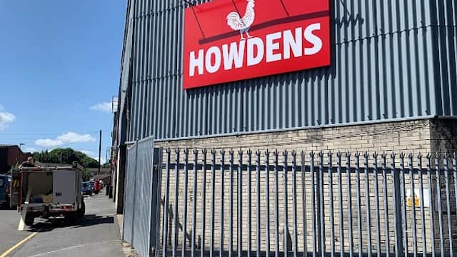 Howdens sign on a corrugated metal building, with a clear blue sky and a fenced area in Sheffield, Yorkshire.