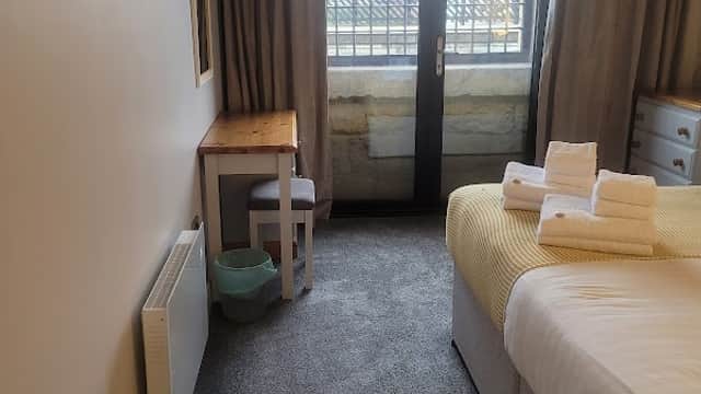 Cozy room with a bed, neatly arranged towels, a desk, chair, and large windows overlooking a scenic view.