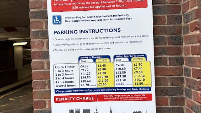 Welcome sign for Coppergate Centre Car Park with parking instructions and fees displayed on a brick wall.
