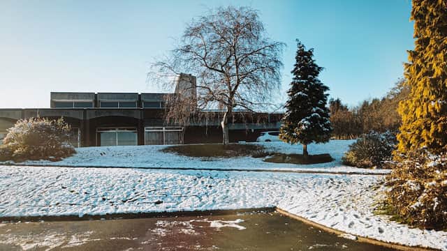 Snow-covered car park at Hutcliffe Wood Crematorium, with a modern building, trees, and clear blue sky.