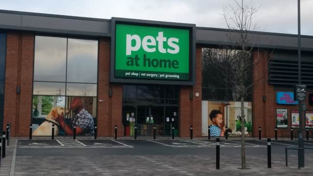 Bright green sign reading "pets at home" on a brick storefront with images of people and pets. Parking area visible.