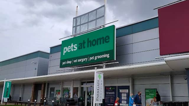 Large green sign reading "pets at home" on a modern pet shop building, with shoppers and cloudy skies above.
