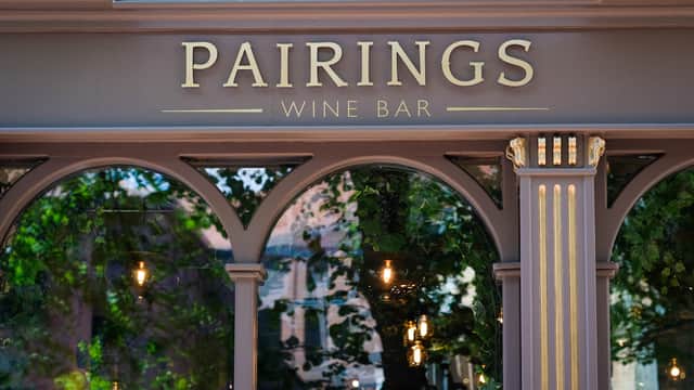 Sign for "Pairings Wine Bar" with elegant lettering and reflections of greenery and lights in the windows.