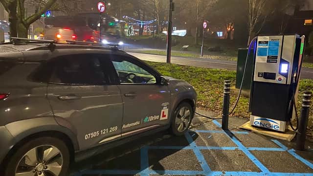 A grey car parked in a designated space near an electric vehicle charging station at night.
