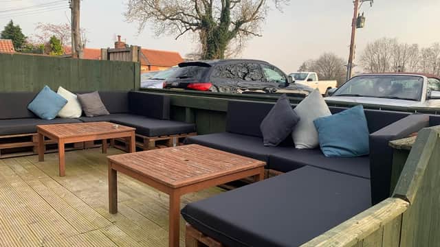 Outdoor seating area with dark sofas and wooden tables, surrounded by trees and parked cars in Great Smeaton, Yorkshire.