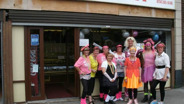 A group of cheerful bakers in colorful outfits stands outside Brook Bakery Ltd, with balloons and a welcoming storefront.