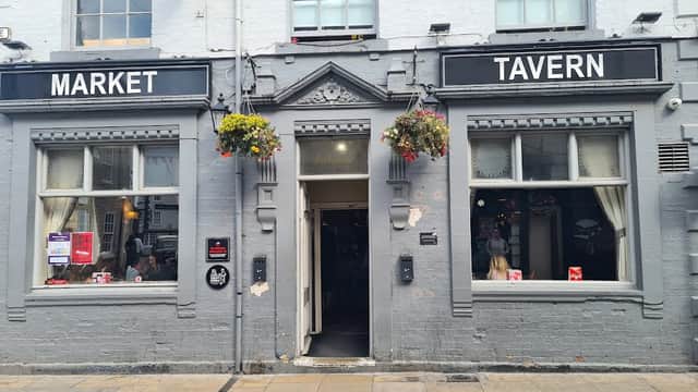 Exterior of Market Tavern, a bar in Plompton, Yorkshire, featuring hanging flower baskets and large windows.
