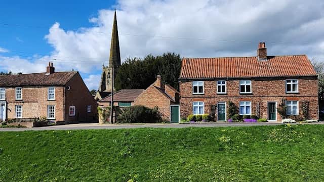 Bishop Wilton Village Hall with stone buildings, a church spire, and a grassy foreground under a blue sky.