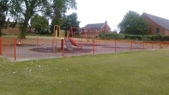 Playground with swings and slides, surrounded by a red fence and green grass, near residential houses in Castleford.