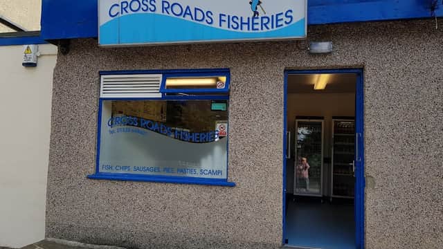Sign for "CROSS ROADS FISHERIES" above a shop entrance with a blue and grey exterior. Windows display menu items.