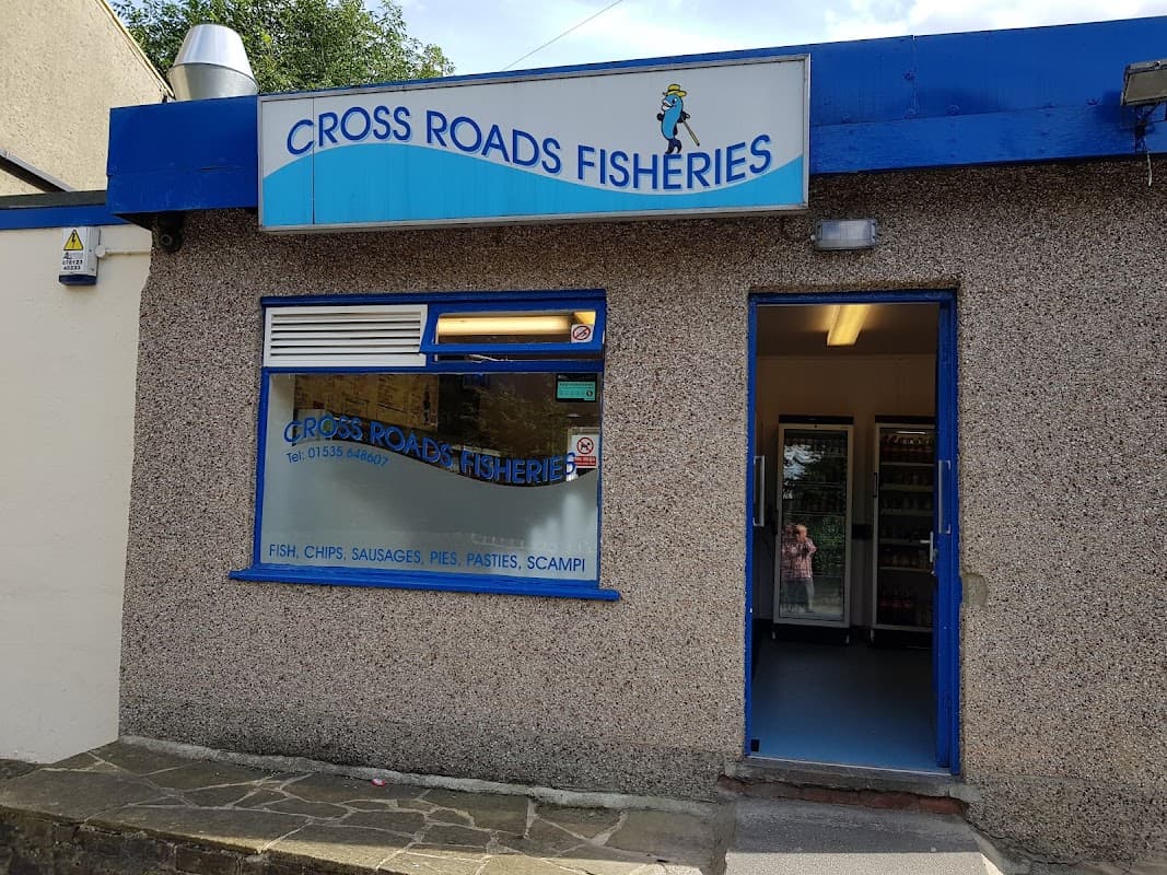 Sign for "CROSS ROADS FISHERIES" above a shop entrance with a blue and grey exterior. Windows display menu items.