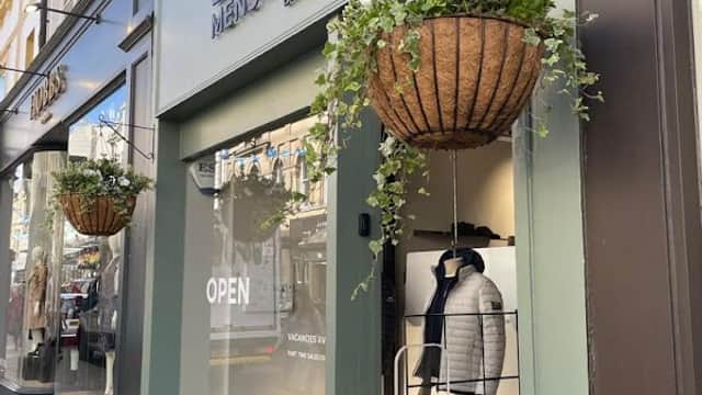 Lynx Menswear shopfront with hanging flower baskets, open sign, and stylish men's clothing displayed inside.