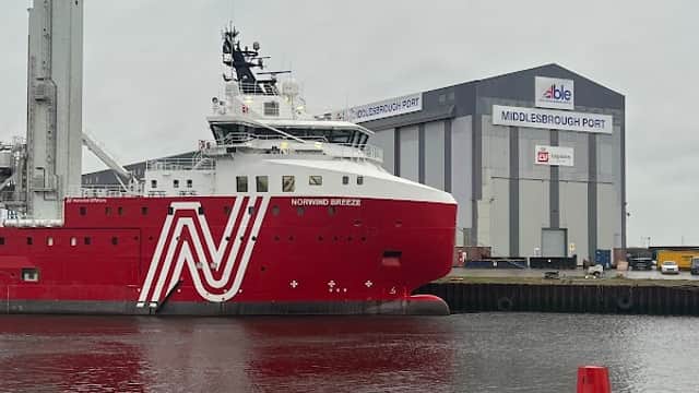 Red and white ship named "NORTHING BREEZE" docked near a large warehouse at Middlesbrough Port under a cloudy sky.