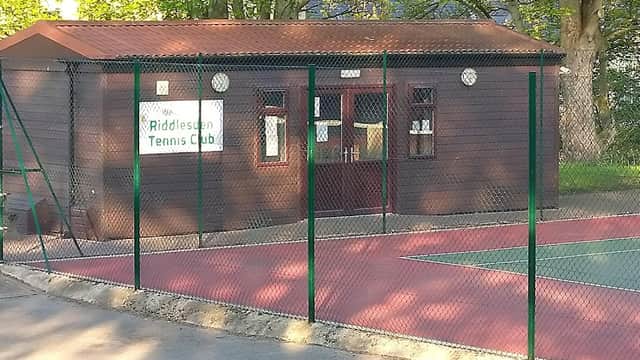 Riddlesden Tennis Club building with a fenced court area and trees in the background.