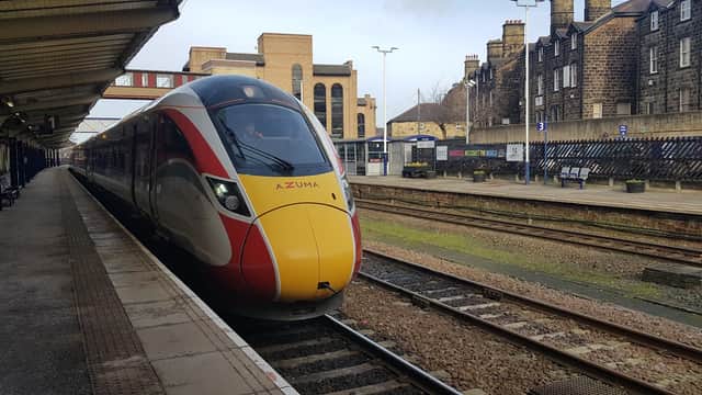A red and yellow train at Harrogate railway station, with stone buildings and tracks visible in the background.