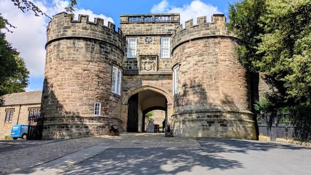 Historic stone entrance with towers, trees lining the path, and a blue sky in Skipton Castle Woods, Yorkshire.