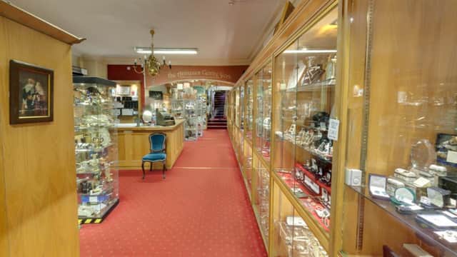 Elegant antiques showroom with glass display cases, red carpet, chandelier, and vintage furniture, creating a classic atmosphere.