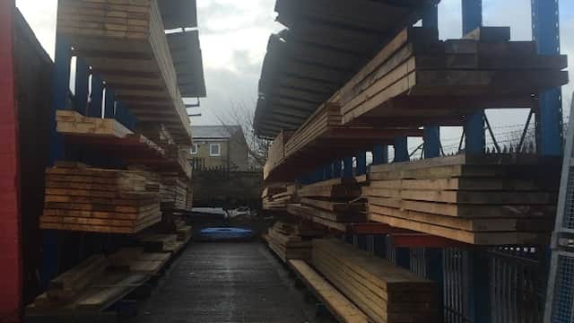 Timber racks filled with wooden planks, lined along a pathway at Manningham Timber and Roofing in Bradford.