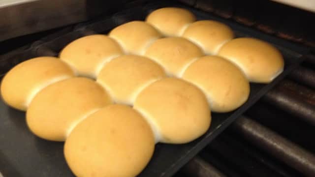 Freshly baked golden rolls arranged neatly on a tray, with a baking oven in the background.