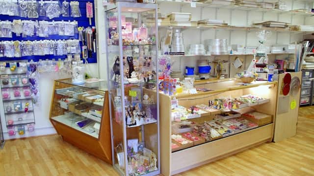 Brightly lit bakery shop interior with display cases filled with cake decorations and baking supplies on wooden flooring.
