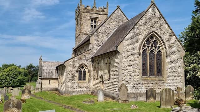 Historic Stonegrave Minster with stone walls, a tower, and a graveyard under a clear blue sky.