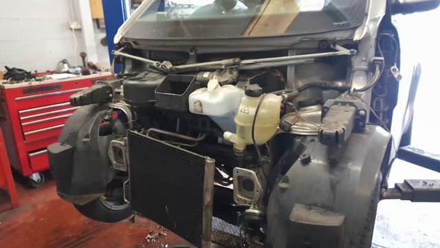 Car with exposed front components in a garage, tools and red tool chest visible in the background.