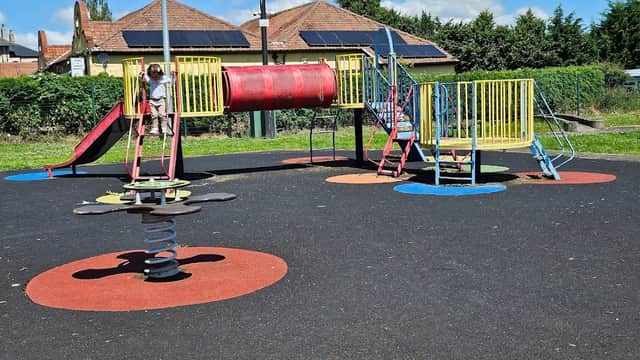 Colorful playground equipment with a slide, tunnel, and spring rider on a rubber surface under a clear blue sky.