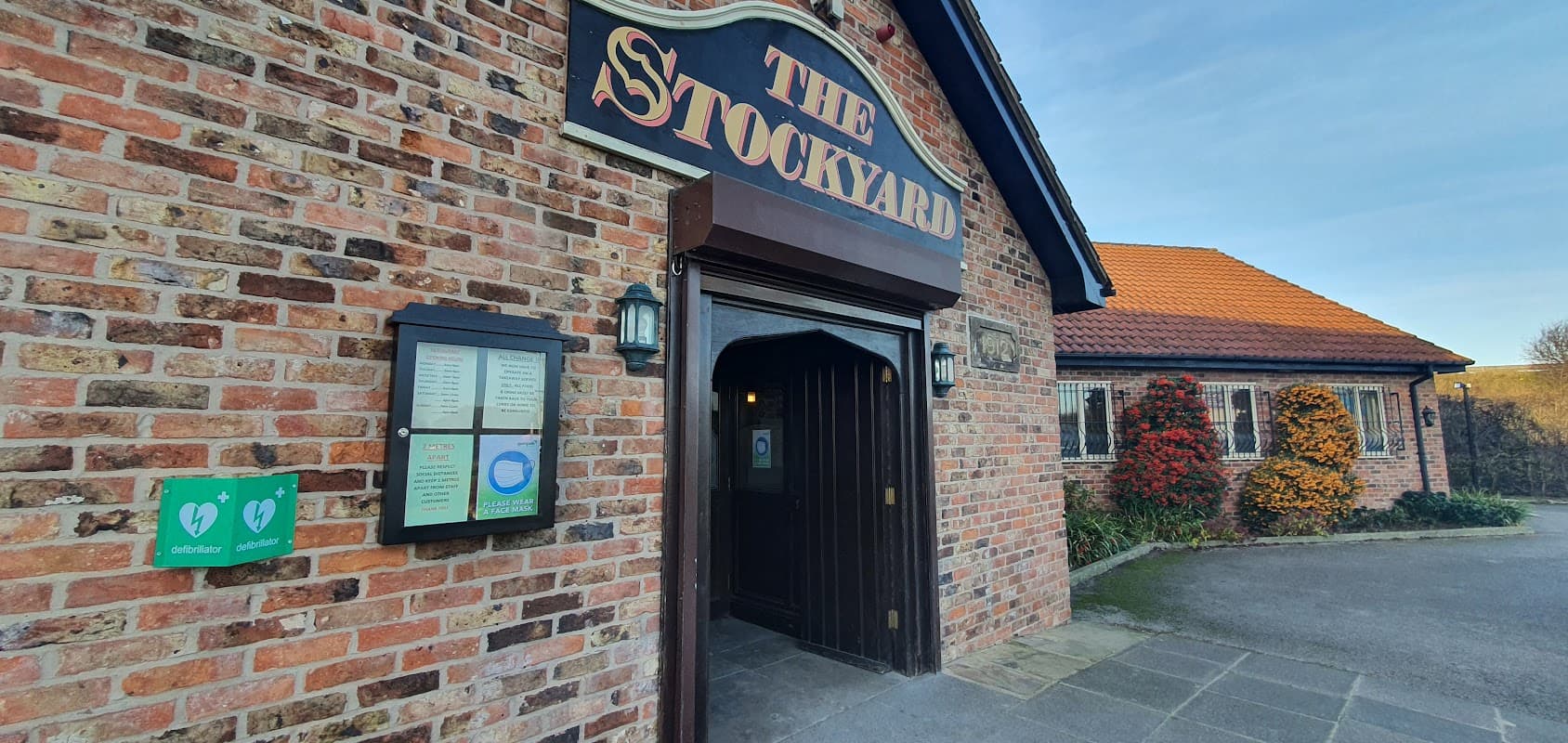 Entrance to The Stockyard Truckstop with brick exterior, menu board, and colorful plants by the doorway.